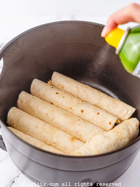 Taquitos being sprayed with oil in the air fryer basket
