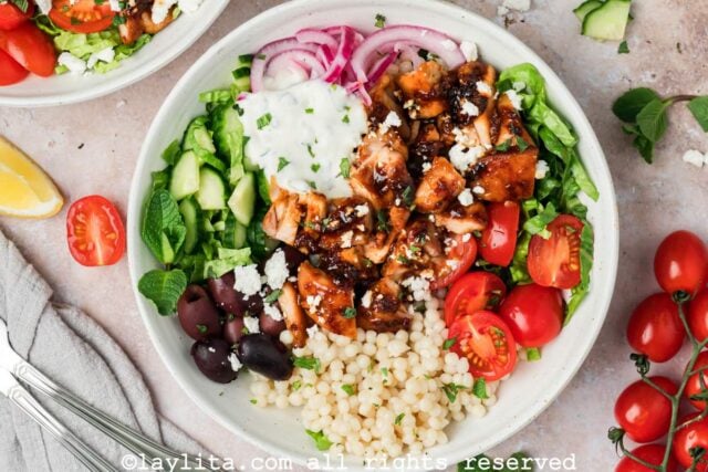 Overhead shot of a honey harissa chicken bowl with vegetables and mint lemon yogurt sauce.