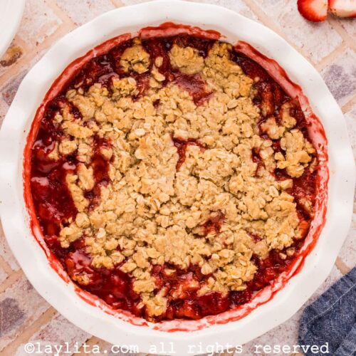 Strawberry Crisp in a white pie dish on a tile countertop with fresh strawberries on the side