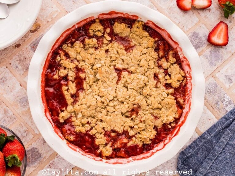 Strawberry Crisp in a white pie dish on a tile countertop with fresh strawberries on the side