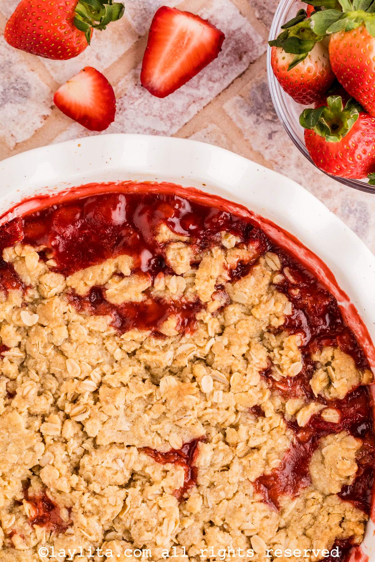 Partial closeup of a white pie dish with strawberry crisp, with additional strawberries on the side