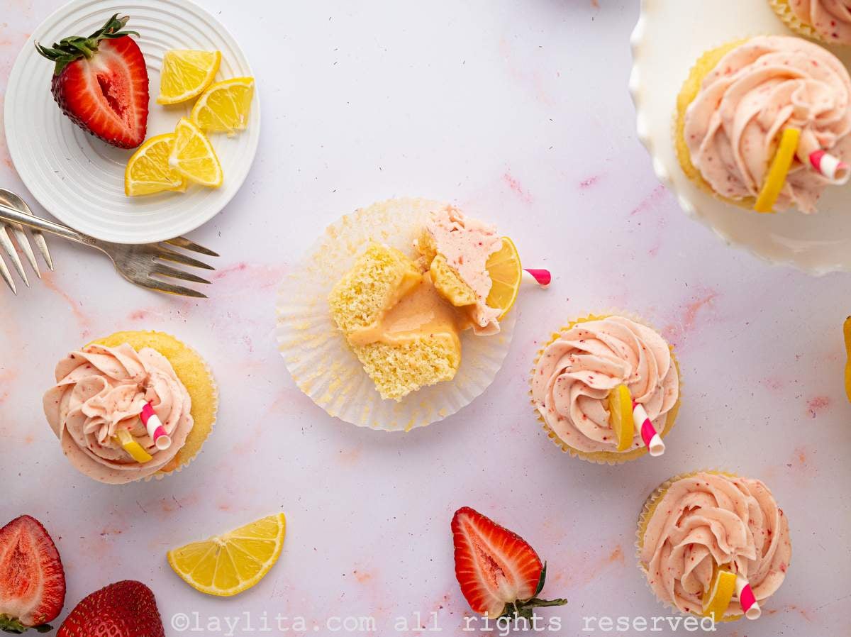 Overhead view of several strawberry lemon filled cupcakes with one of them cut in half to show the filling