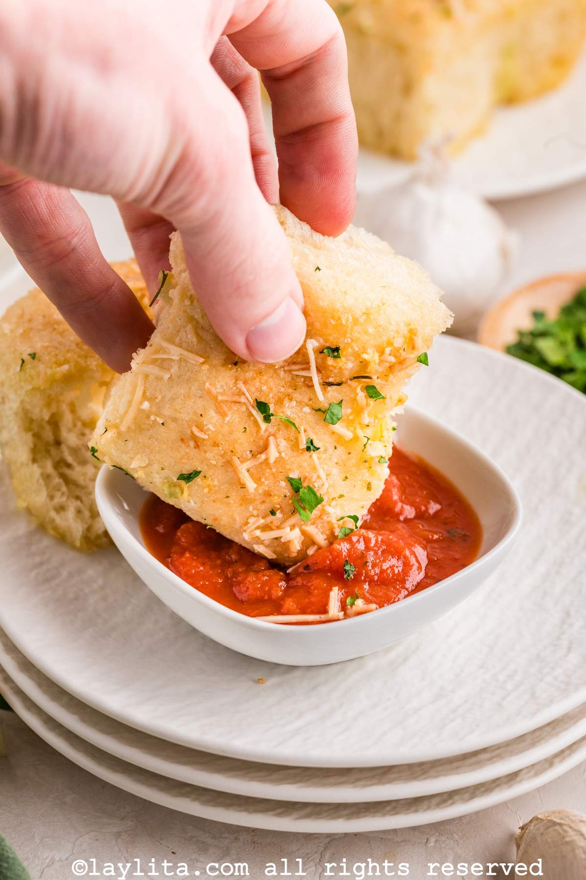 Hand dipping a cheese stuffed dinner roll into marinara sauce.