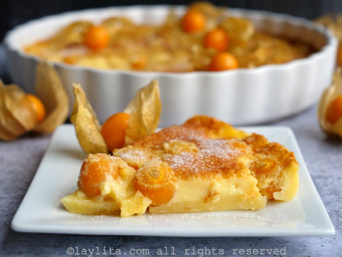 Side view of a slice of uvilla clafoutis with the rest of the clafoutis in the background.
