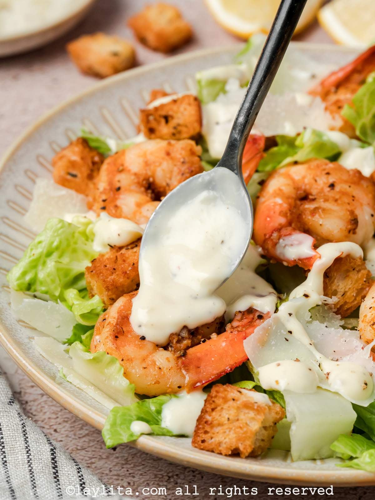Spoon drizzling Caesar dressing over a bowl of Shrimp Caesar salad.