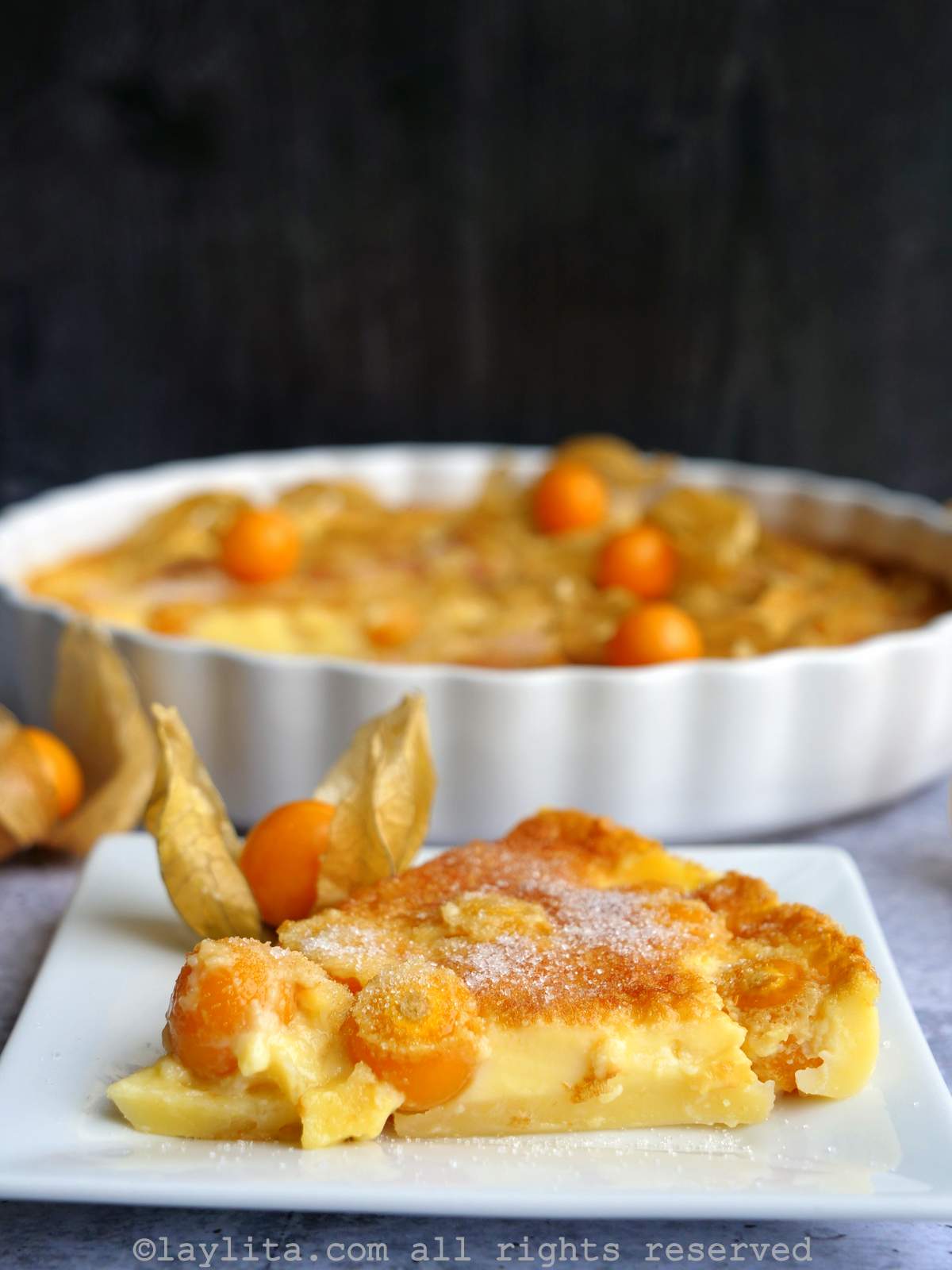 Side view of a slice of a goldenberry or physalis clafoutis with the rest of the clafoutis in the background.