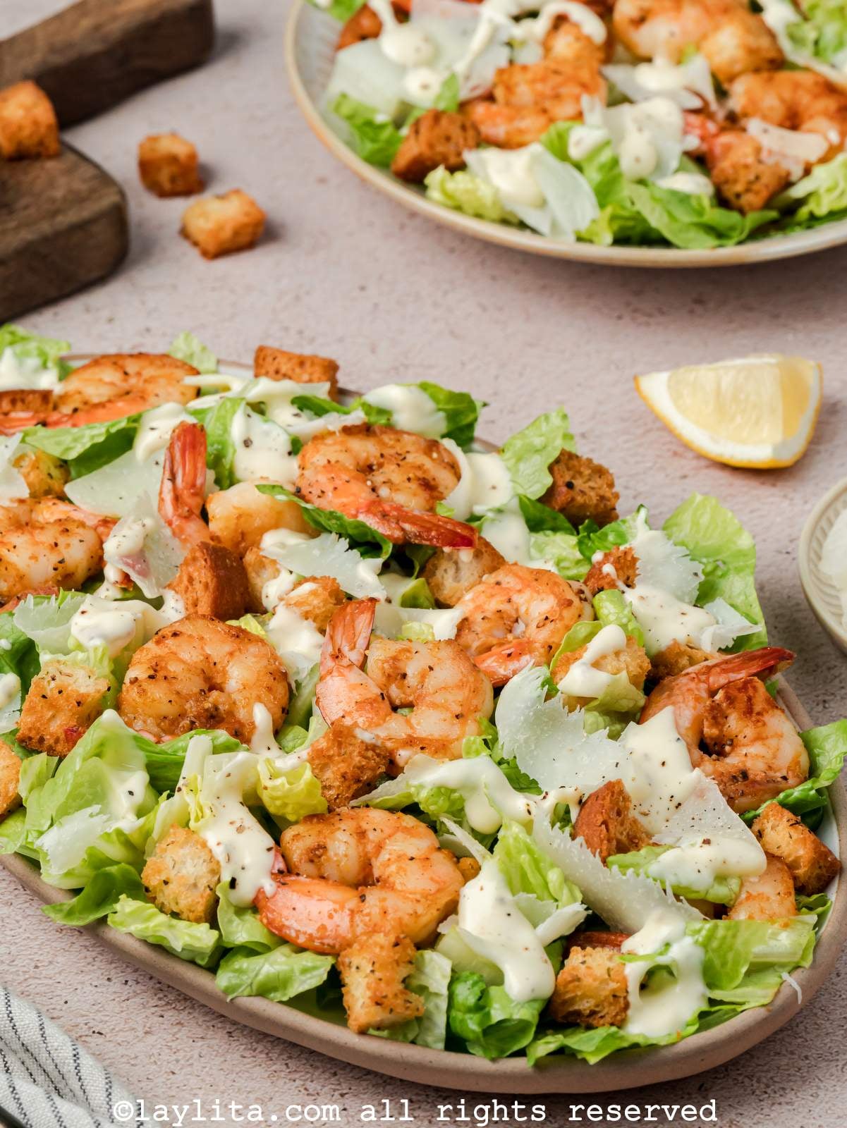 Platter of shrimp Caesar salad with a bowl of salad in the background.