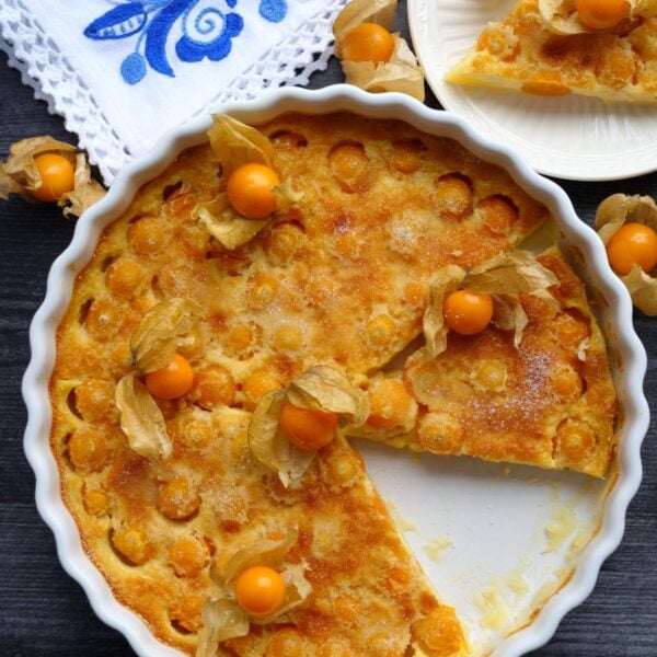 Overhead shot of uvilla clafoutis in a white tart pan with fresh uvillas on top as garnish.