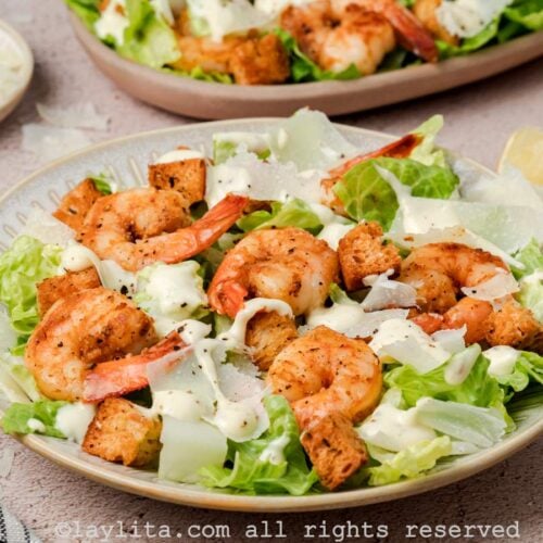 Side view of shot of a bowl served with shrimp Caesar salad with a platter of salad in the background