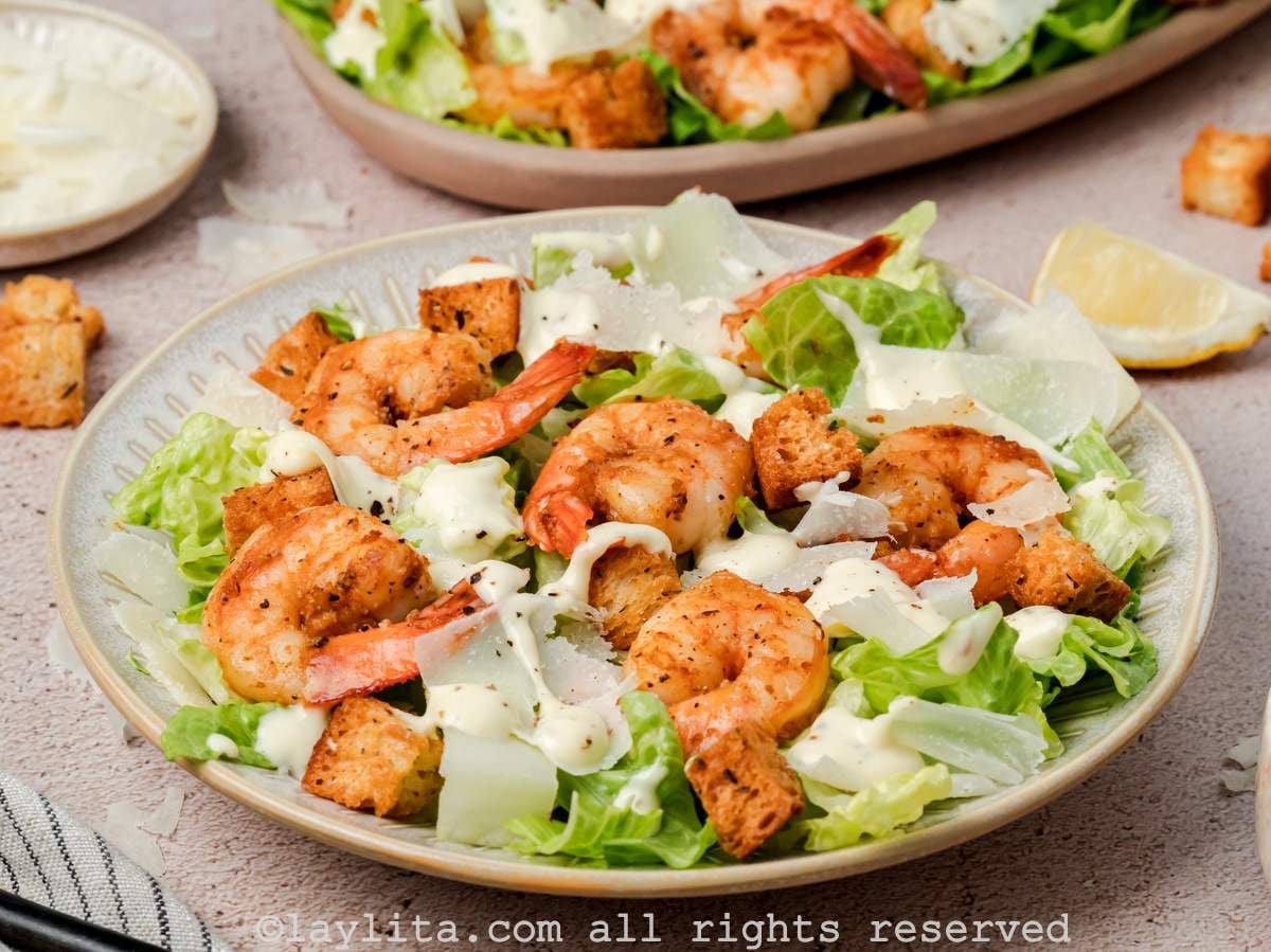 Side view of shot of a bowl served with shrimp Caesar salad with a platter of salad in the background