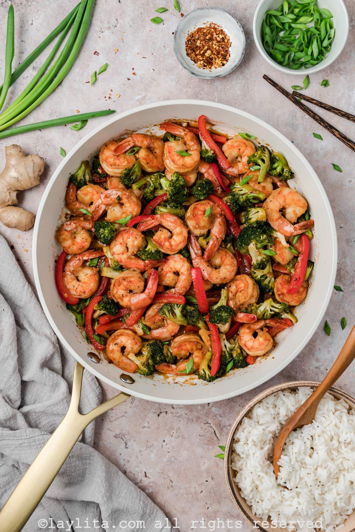 Overhead shot of shrimp broccoli stir fry in a skillet with a bowl of rice on the side