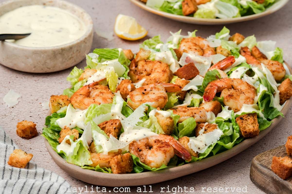 Side view of a platter of Shrimp Caesar salad with a bowl of dressing next to it
