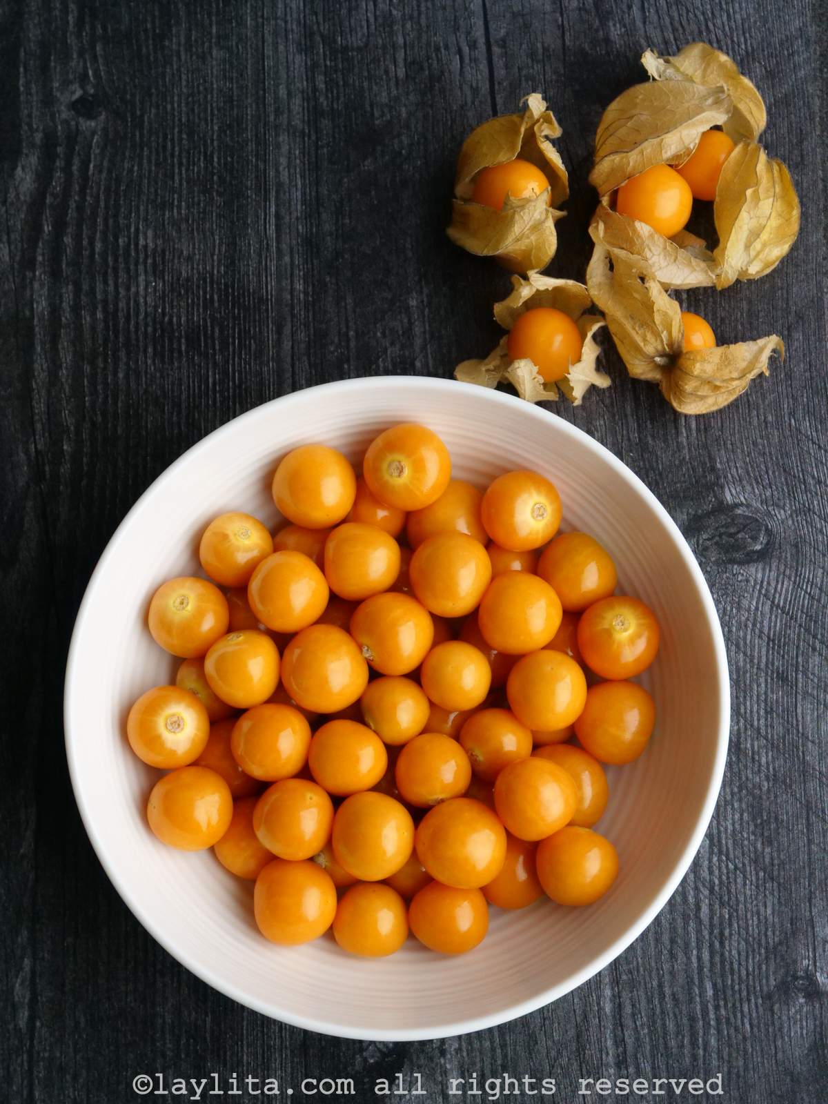 A white bowl full of husked goldenberries or physalis with some additional fruits with husks on the side