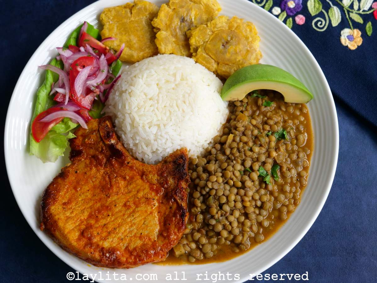 Overhead shot of an achiote pork chop served with rice and lentils on a blue and white plate on a white background.