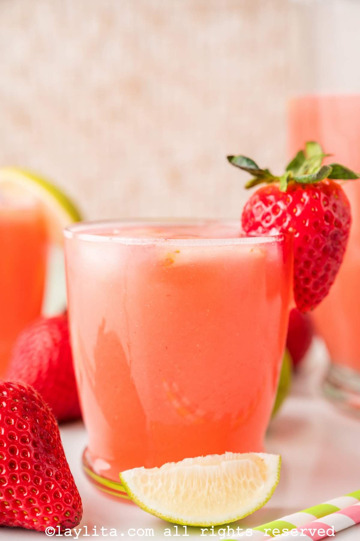 Side view of a glass of strawberry agua fresca with a lime wedge in front of it.