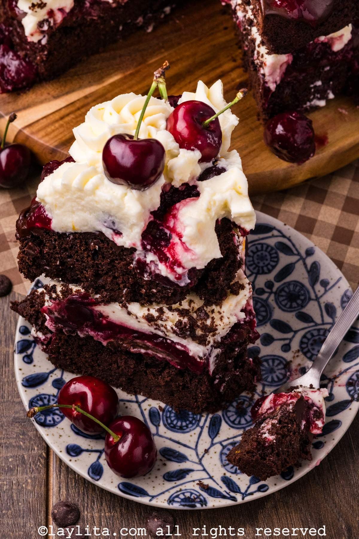 A slice of Black Forest cake on white and blue plate with the rest of the cake in the background