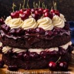 A layered Black Forest cake topped with whipped mascarpone frosting and cherries on a wooden platter with more cherries on the side