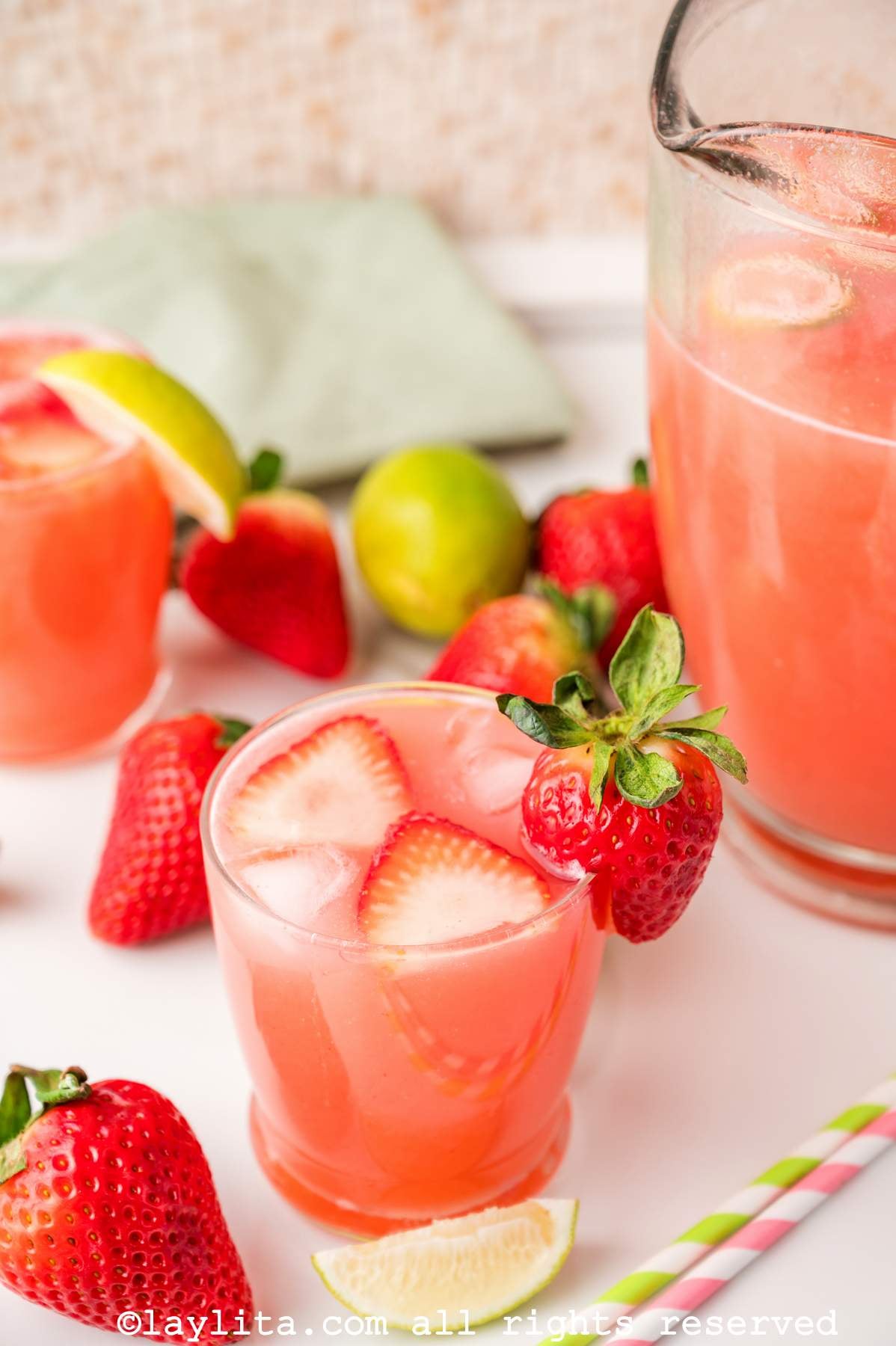 Glass of agua fresca with fresh strawberries on top, next to the pitcher of agua fresca.