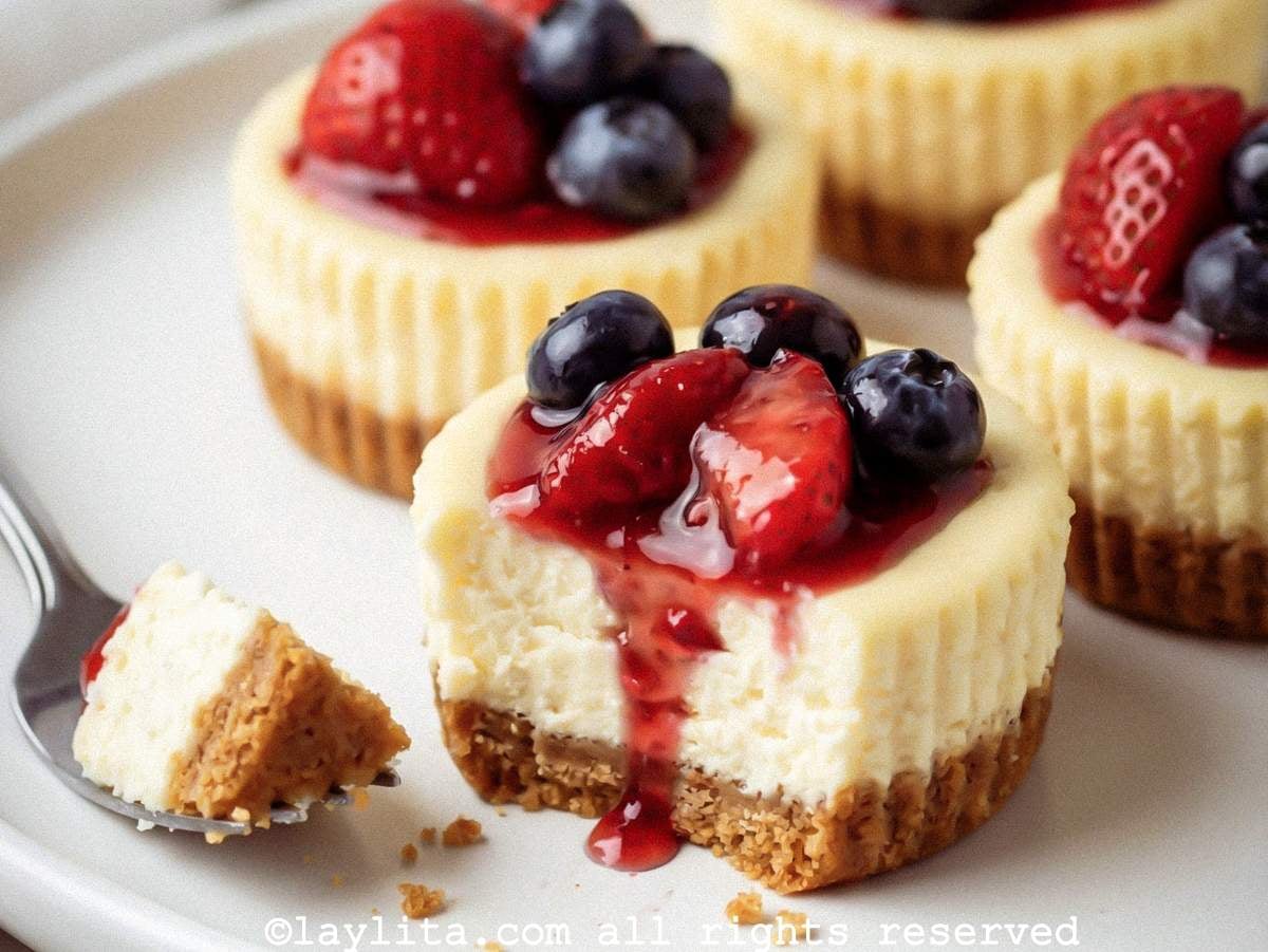 Closeup of a mini cheesecake topped with berries on a plate with a bite taken from it.