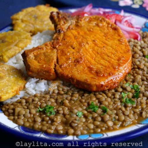 Achiote pork chop on a bed of rice and lentils on a blue and white plate with a blue background.