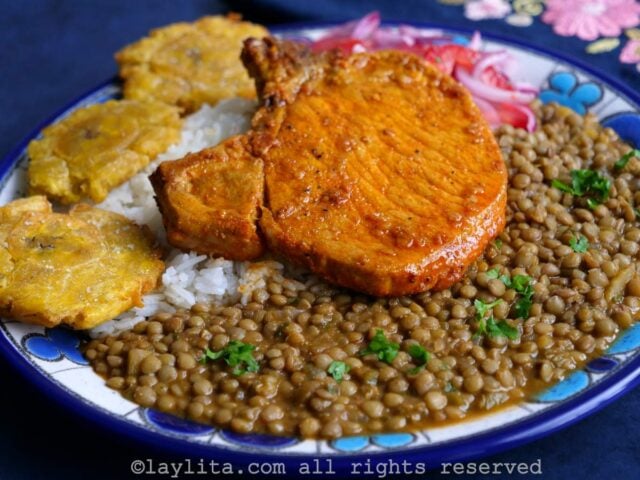Achiote pork chop on a bed of rice and lentils on a blue and white plate with a blue background.