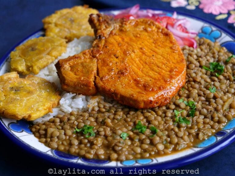 Achiote pork chop on a bed of rice and lentils on a blue and white plate with a blue background.