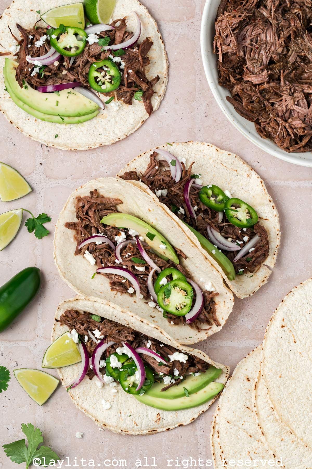 Overhead view of three beef barbaco tacos with another taco in the background and a bowl of shredded beef on the side
