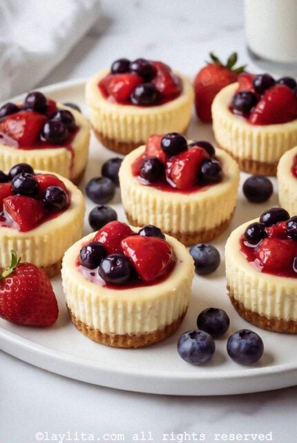 Mini cheesecakes on a plate with fruit scattered around the plate.
