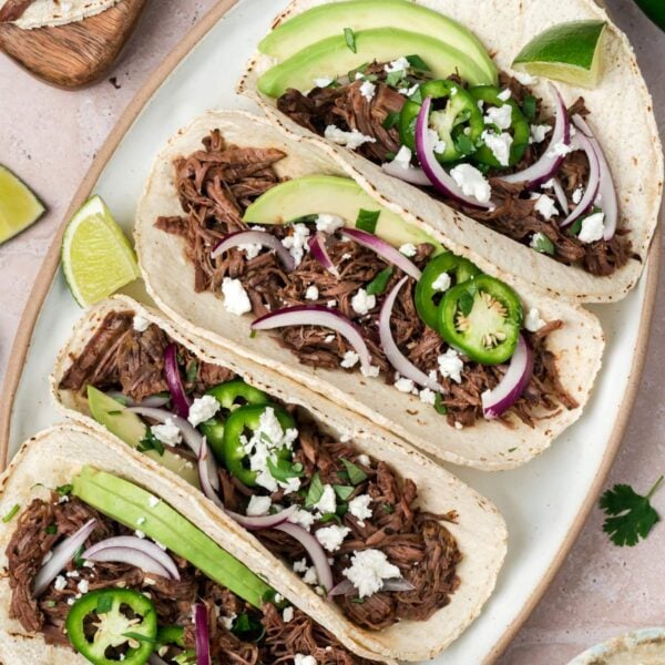 Overhead shot of four barbacoa tacos garnished with onions and jalapenos on a plate.