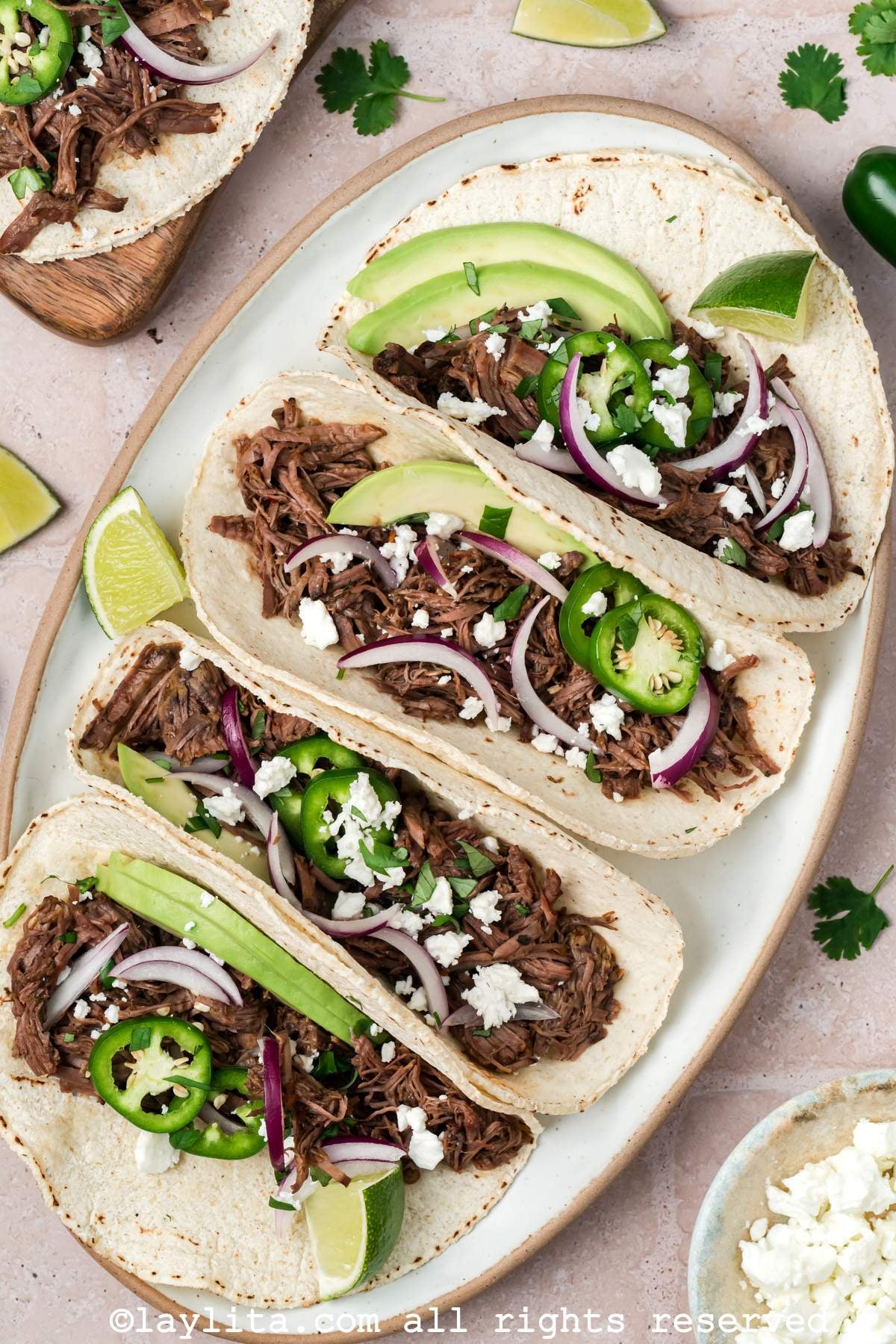 Overhead shot of four barbacoa tacos garnished with onions and jalapenos on a plate. 