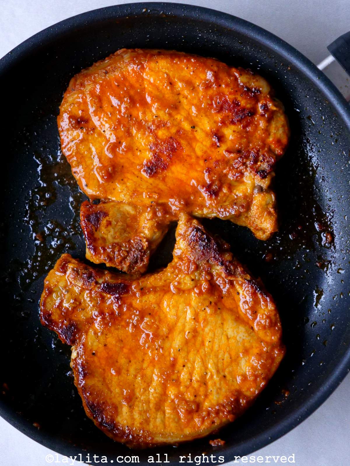 Overhead shot of two achiote pork chops cooking in a skillet