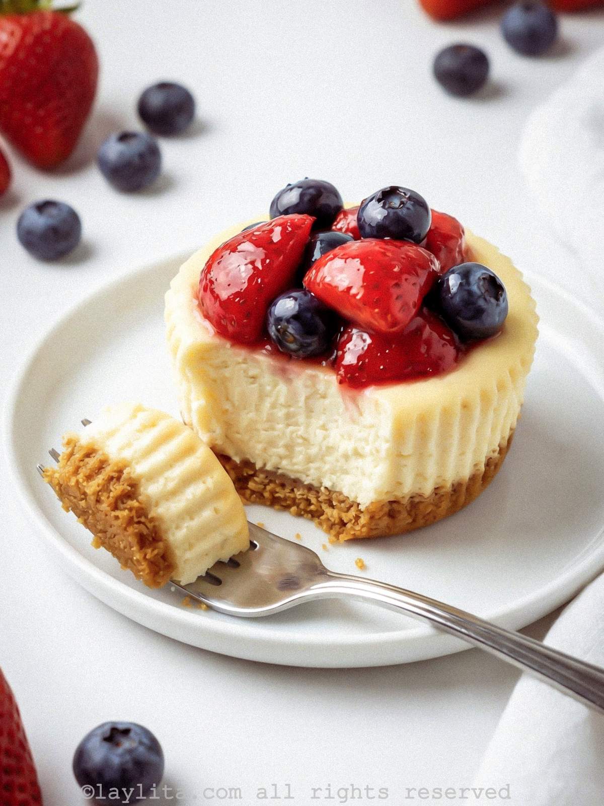 Mini cheesecake topped with berries on a plate with a bite taken from it.