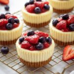 Mini cheesecakes topped with berries on a cooling rack.