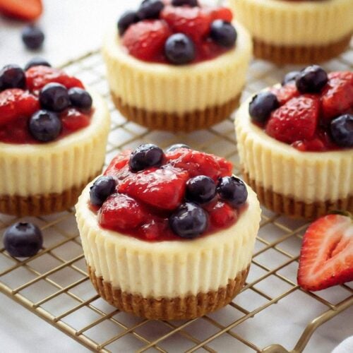 Mini cheesecakes topped with berries on a cooling rack.