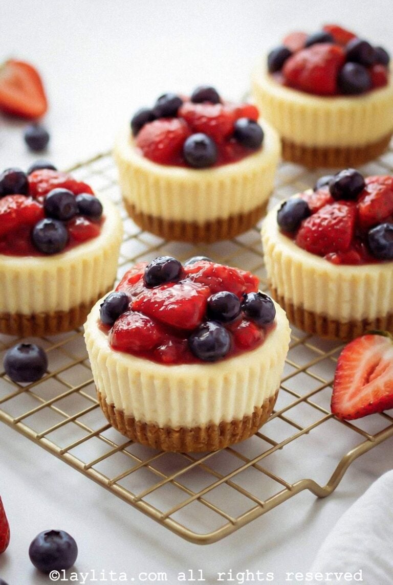 Mini cheesecakes topped with berries on a cooling rack.