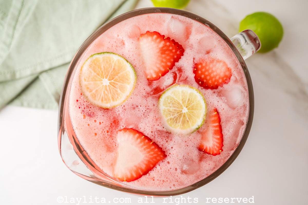 Overhead view of a pitcher of strawberry agua fresca with fresh strawberries and limes on top