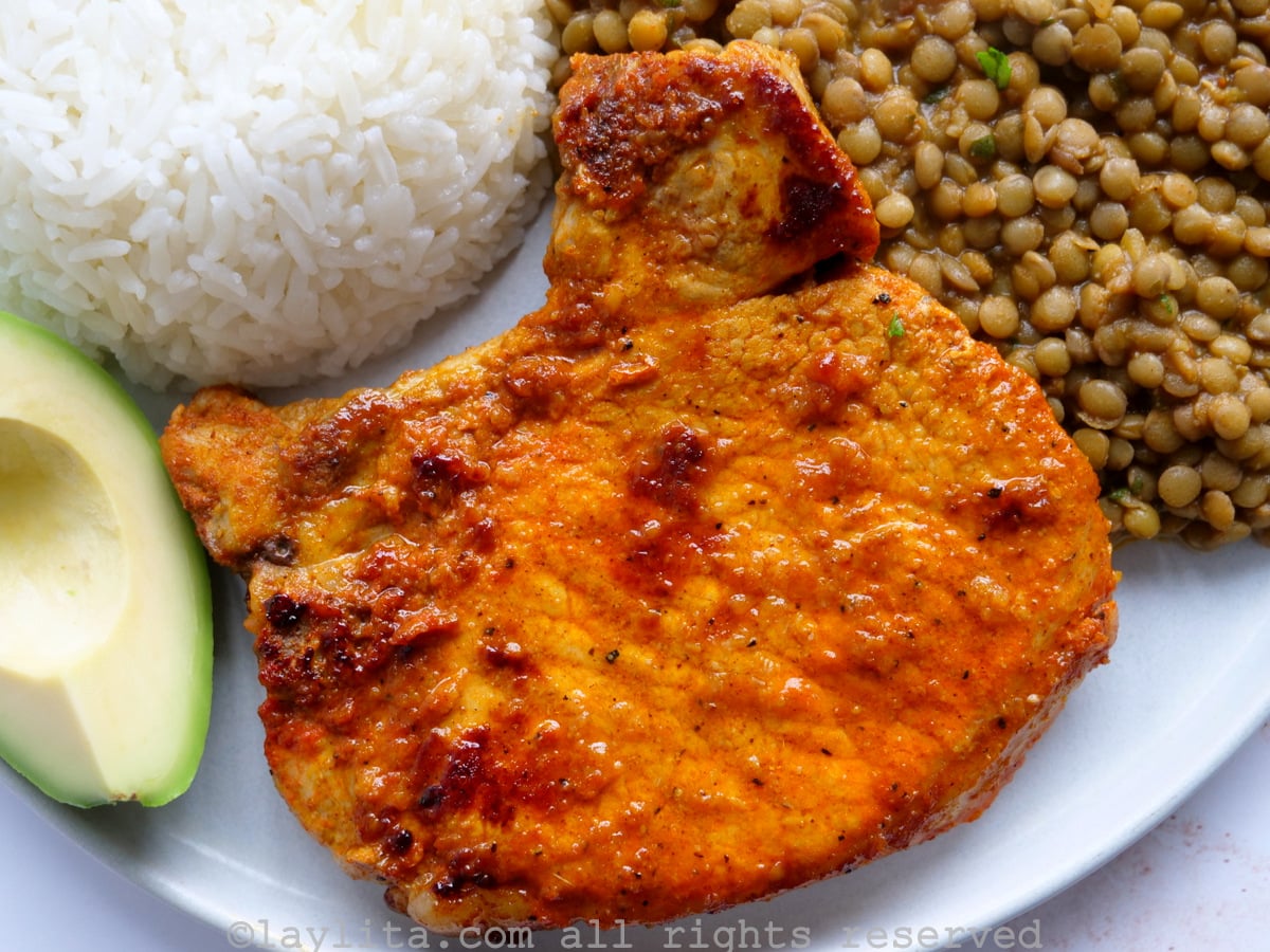 Overhead shot of an achiote marinated cooked pork chop, close up, on a plate with rice, lentils and avocado