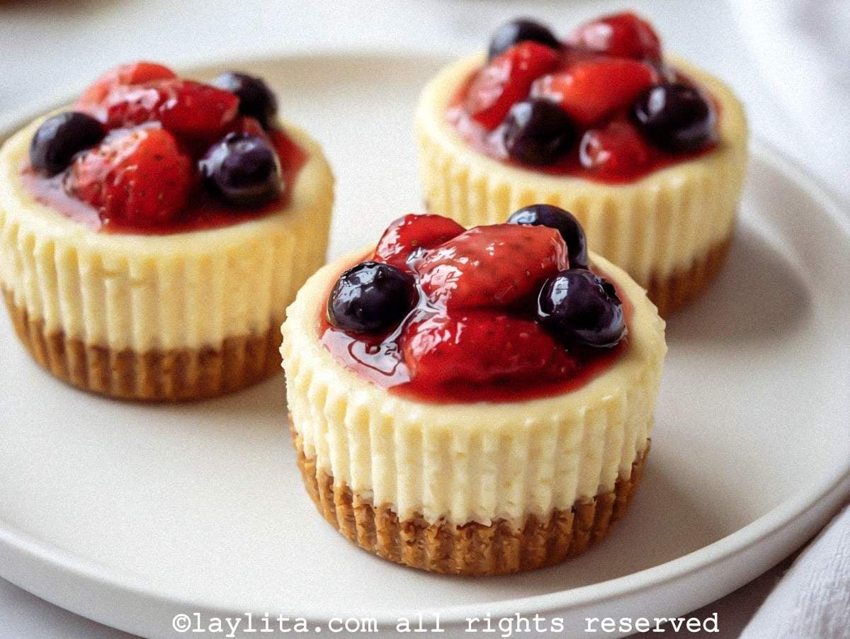 Side view of a platter of mini cheesecakes with berry filling on top.