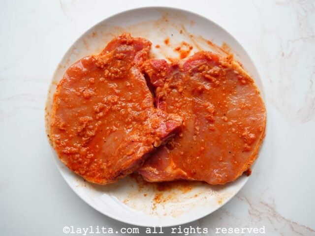 Achiote rubbed pork chops marinating on a white plate