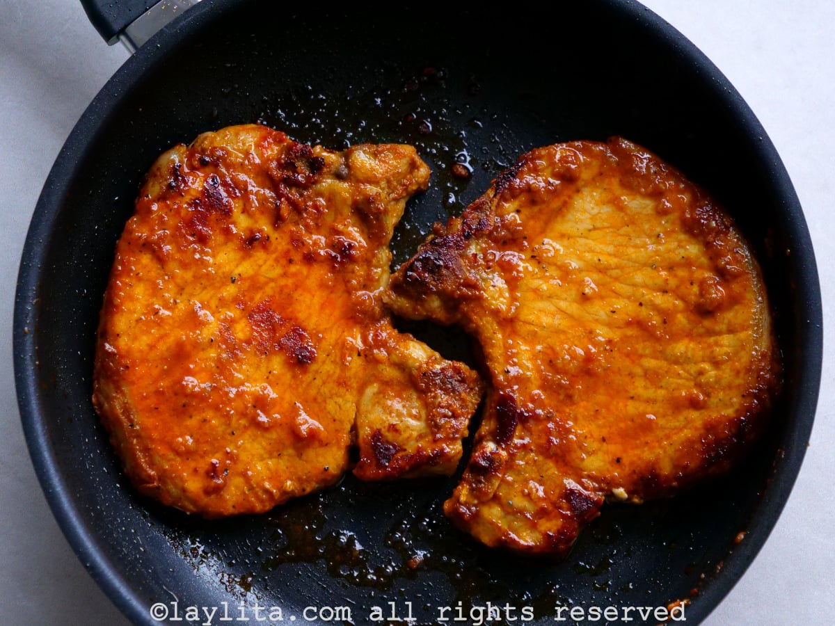 Two achiote pork chops cooking in a pan