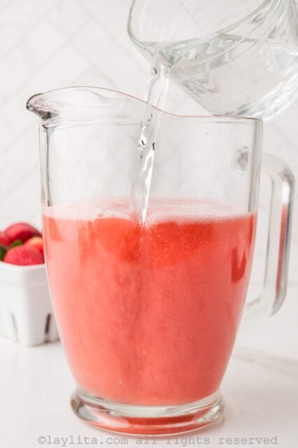 Adding water to the strawberry agua fresca in a pitcher