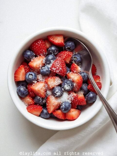 Blueberries and sliced strawberries with sugar in a white bowl