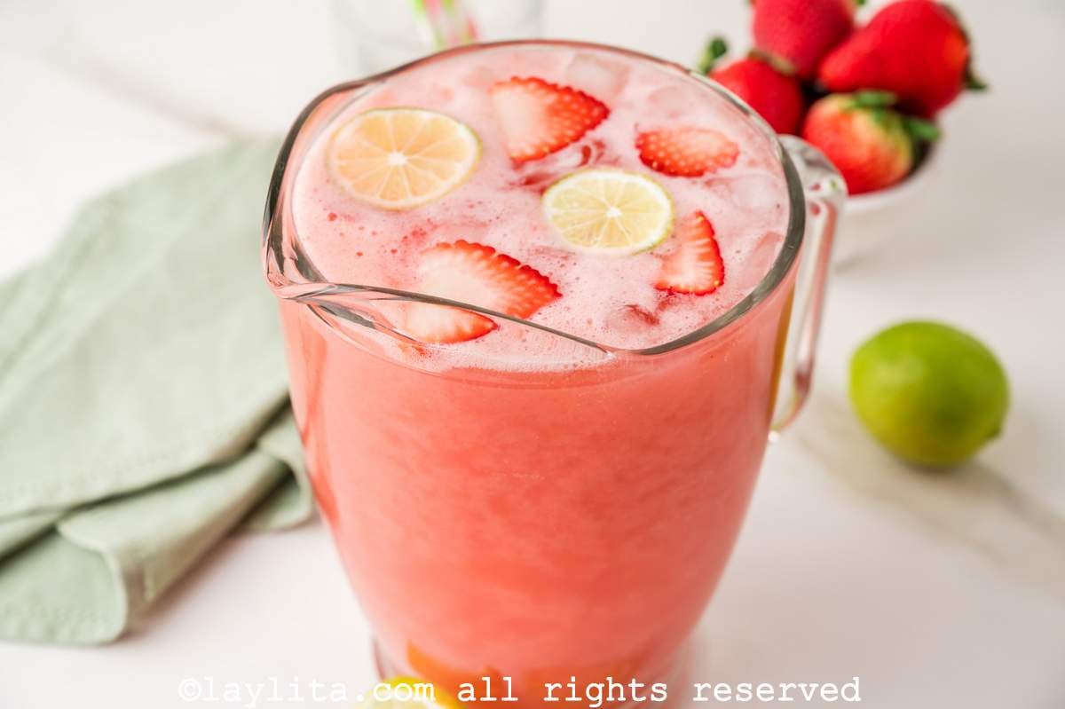 Pitcher of strawberry agua fresca with fresh strawberries and limes on top