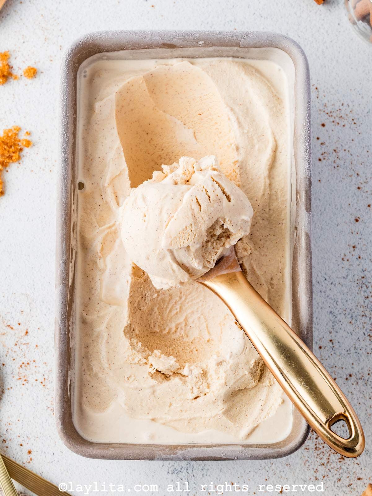 Overhead view of cinnamon ice cream in a loaf pan with an ice cream scoop in the middle
