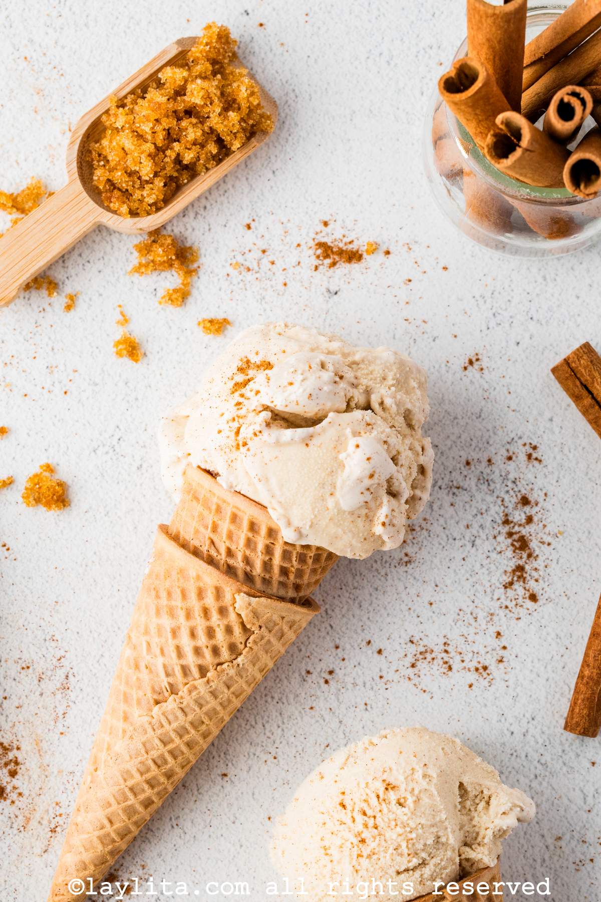 Overhead shot of a scoop of cinnamon ice cream on a cone next to cinnamon sticks.