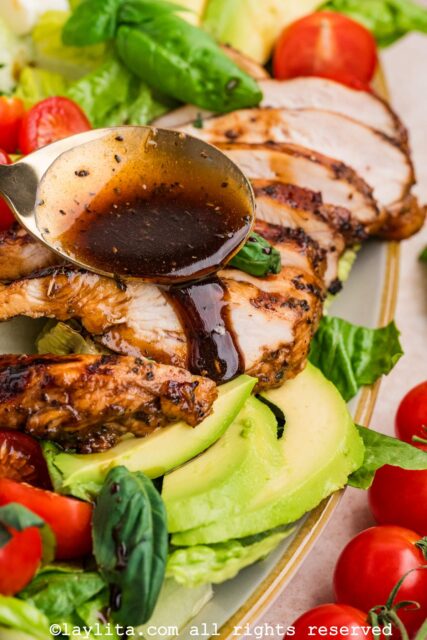 Closeup shot of a spoon drizzling balsamic dressing over sliced chicken breasts on a salad platter