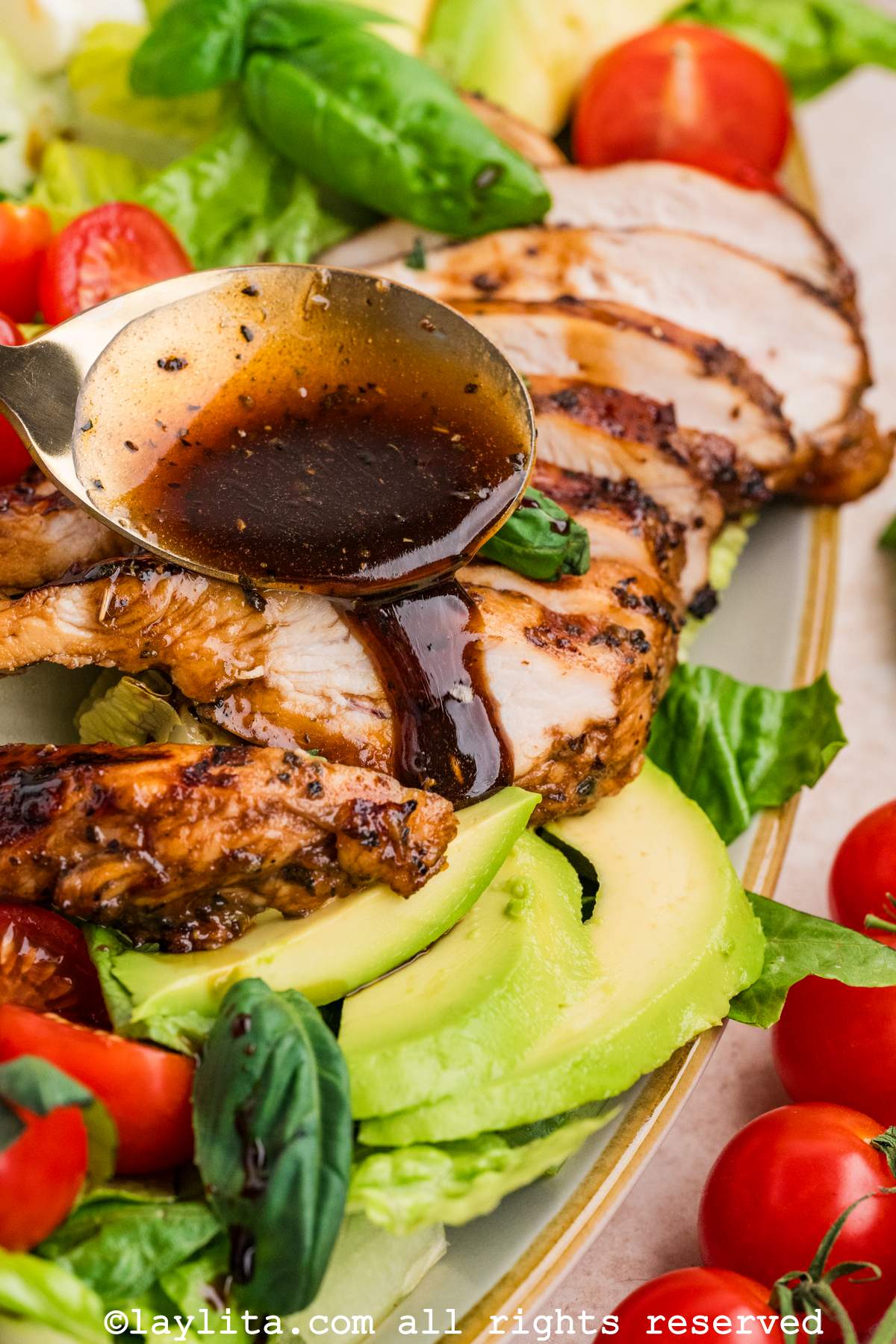 Closeup shot of a spoon drizzling balsamic dressing over sliced chicken breasts on a salad platter