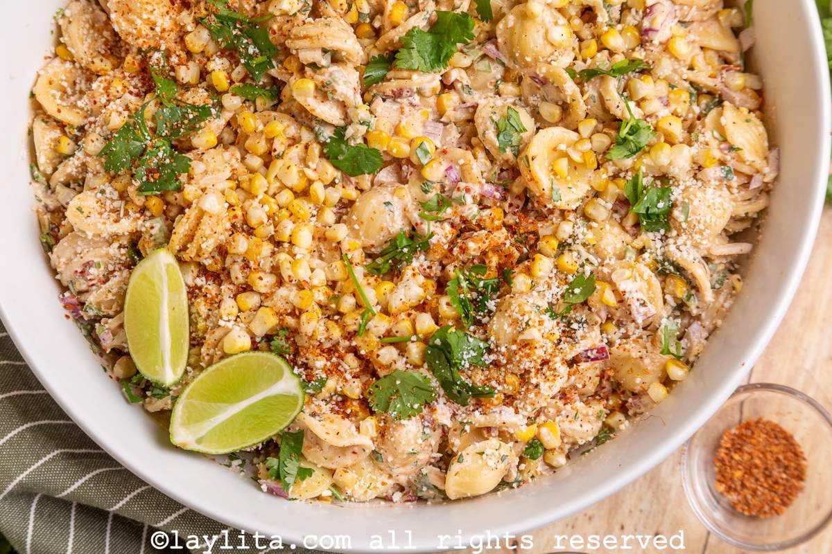 Overhead view of half a bowl of Mexican street corn pasta salad with lime wedges on top and  small bowl of Tajin spice on the side