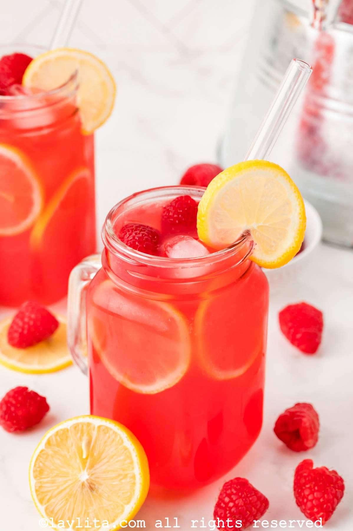 Side view of a jar of raspberry lemonade next to a half of a lemon with another jar in the background