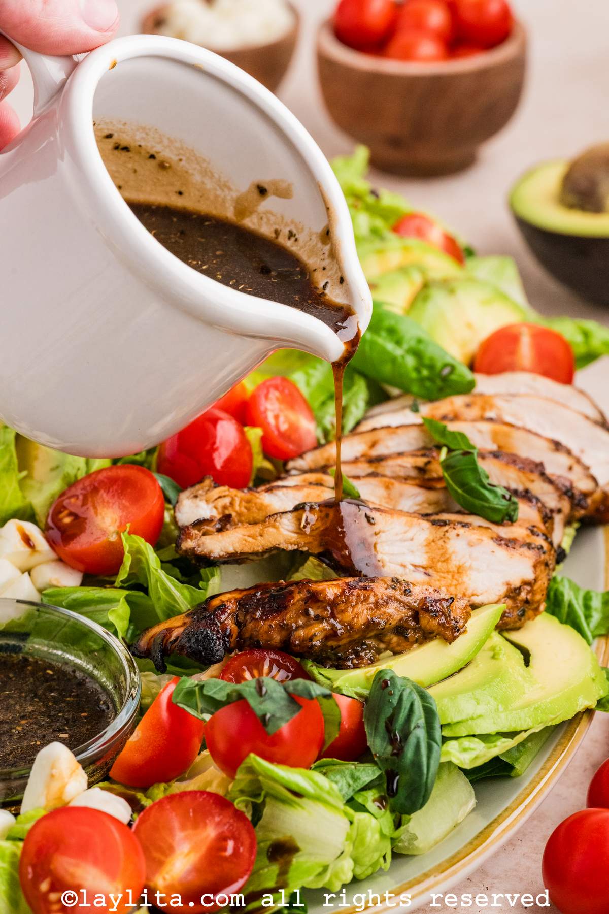 Hand pouring dressing over top sliced chicken on a salad